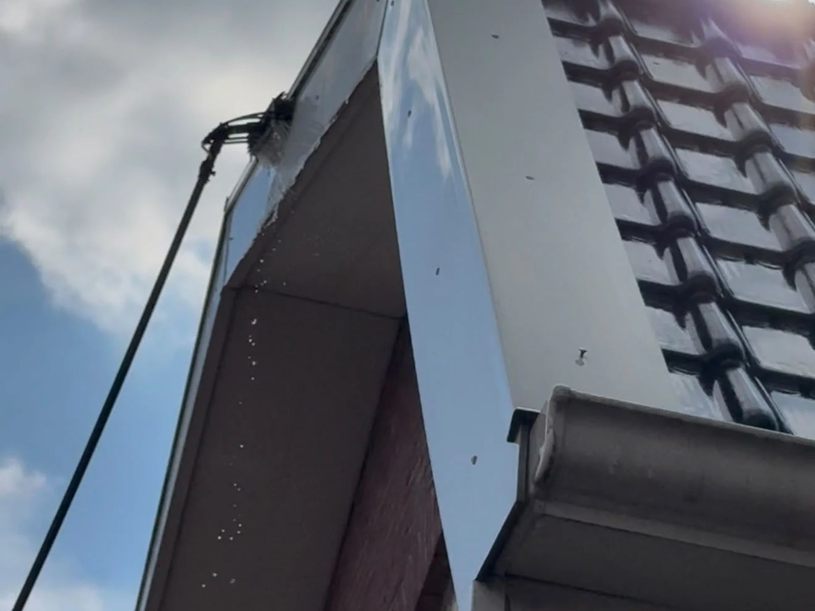 Zijwang van een dakkapel wordt vanaf de grond gereinigd met een borstel aan een telescoopsteel
